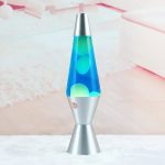 Lâmpada de lava com base metálica prateada e tubo de vidro transparente com cera colorida azul e verde a flutuar.