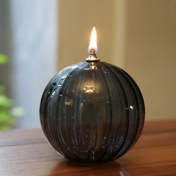 Candeeiro de mesa a óleo em forma de bola de vidro escuro, com chama acesa no topo, colocado numa superfície de madeira.