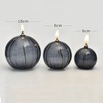 Três candeeiros de mesa a óleo em forma de bolas de diferentes tamanhos, com chamas acesas, medindo 10cm, 8cm e 6cm, com acabamento preto e detalhes dourados.