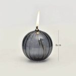 Candeeiro de mesa em forma de bola de vidro escuro com vela acesa no topo, altura de 8cm, com detalhes de vidro transparente e escuro.