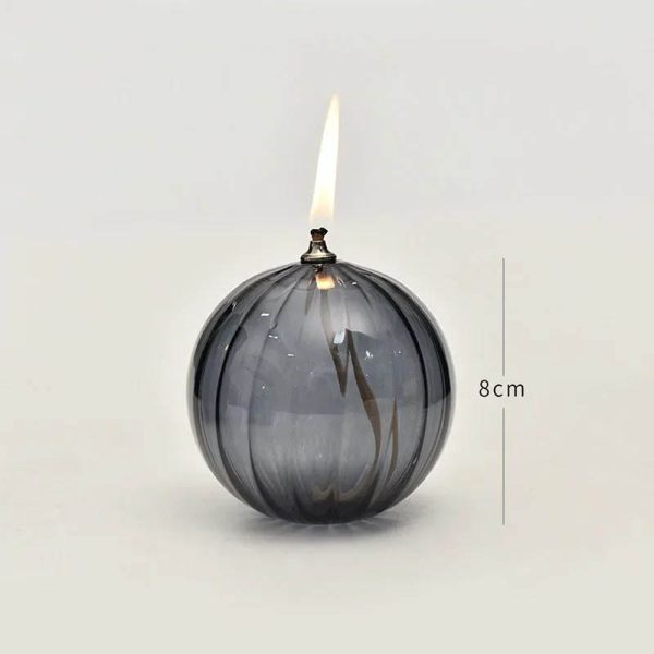 Candeeiro de mesa em forma de bola de vidro escuro com vela acesa no topo, altura de 8cm, com detalhes de vidro transparente e escuro.