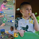 Criança a explorar um kit de insetos com lupa, pinças e recipientes ao ar livre, com outros brinquedos de ciência na mesa.
