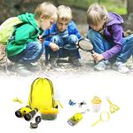 Três crianças explorando ao ar livre com lupa, observando o solo e pequenos objetos, com um kit de exploração científico ao lado.
