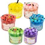Vários potes de slime colorido com diferentes aromas e decorativos, incluindo frutas de plástico, glitter e pérolas, em frascos transparentes com etiquetas temáticas.