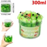 Gelatina de cor verde com pedaços de fruta de plástico decorativa, mostrada em um recipiente de 300ml, com detalhes de fatias de melancia e uvas de plástico.