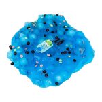 Slime azul com glitter, bolinhas pretas e pequenas flores de plástico, com textura viscosa e brilhante, em uma superfície branca.