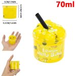 Pequena bola de slime amarelo com rosto sorridente, segurada na mão, com embalagem de 70ml ao fundo, destaque para a textura crocante e cor vibrante.