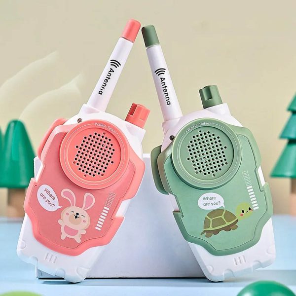 Par de walkie talkies infantis em cores pastel, com antenas ajustáveis e desenhos de coelho e tartaruga, em fundo com árvores de brinquedo.