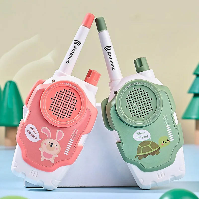 Par de walkie talkies infantis em cores pastel, com antenas ajustáveis e desenhos de coelho e tartaruga, em fundo com árvores de brinquedo.