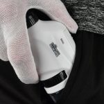 Microscópio de bolso branco com lente ajustável, sendo segurado por uma mão com luva de proteção, próximo da cintura de uma pessoa.