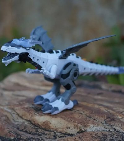 Robô dinossauro branco com detalhes cinzentos, com cabeça articulada, cauda longa e patas robustas, posicionado sobre tronco de árvore ao ar livre.