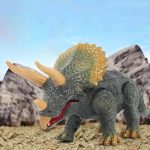 Brinquedo de dinossauro Tricerátopo com chifres e escamas, em ambiente de paisagem rochosa ao ar livre.
