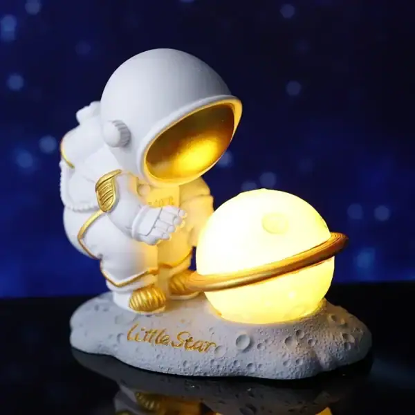 Miniatura de astronauta com capacete dourado a segurar um planeta com anel, sobre uma base lunar com a inscrição "Little Star".