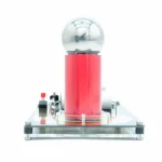 Gerador de Van de Graaff com esfera de metal transparente e base metálica, usado para demonstrações de eletricidade estática.