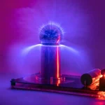 Esfera de plasma com raios de luz azul, roxa e vermelha, sobre base de metal, com efeito de brilho e energia visível dentro da esfera.