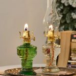 Candeeiro a óleo antigo com base de vidro verde e cúpula de vidro transparente, aceso, em ambiente decorado com árvore de Natal ao fundo.