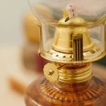 Candeeiro a óleo antigo com vidro transparente, base de metal dourado e mecanismo de ajuste de chama.