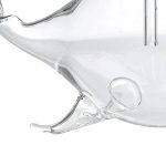 Detalhe de uma escultura de vidro transparente representando uma baleia, com foco na cauda e corpo, sobre fundo branco.