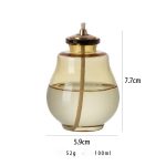 Candeeiro a óleo com corpo de vidro transparente, mecha de algodão e tampa de metal dourado, altura de 7,7cm, diâmetro de 5,9cm, peso de 52g, capacidade de 100ml.
