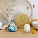 Esponja de limpeza, ovos brancos, vela acesa, folhas secas e elementos decorativos em fundo claro.