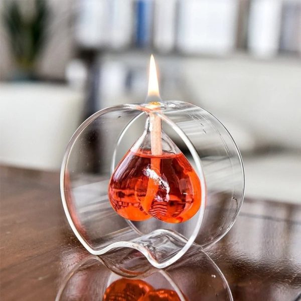 Candeeiro a óleo com forma de coração, com chama acesa, colocado numa superfície de madeira, com fundo de sala de estar.