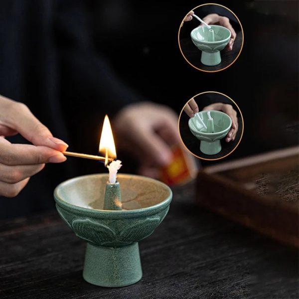 Pessoa acende uma vela de cera numa base de cerâmica verde, com detalhes decorativos, enquanto outra pessoa segura uma tigela de cerâmica com uma vela acesa.