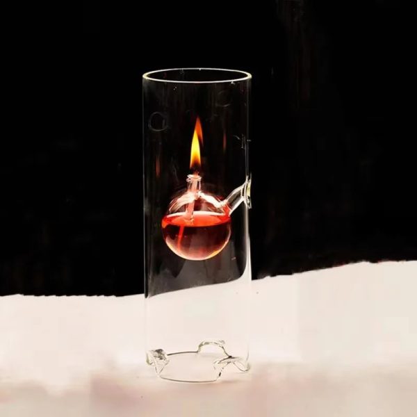 Vidro de laboratório com óleo vermelho e chama acesa, visto de lado, com fundo escuro.