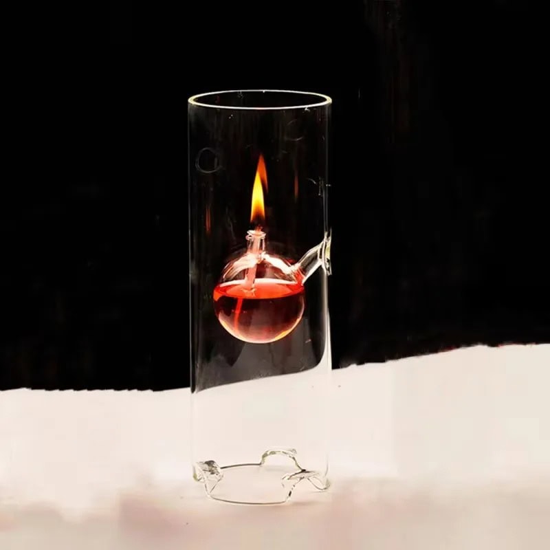 Experimento de laboratório com óleo e fogo Vidro de laboratório com óleo vermelho e chama acesa, visto de lado, com fundo escuro.