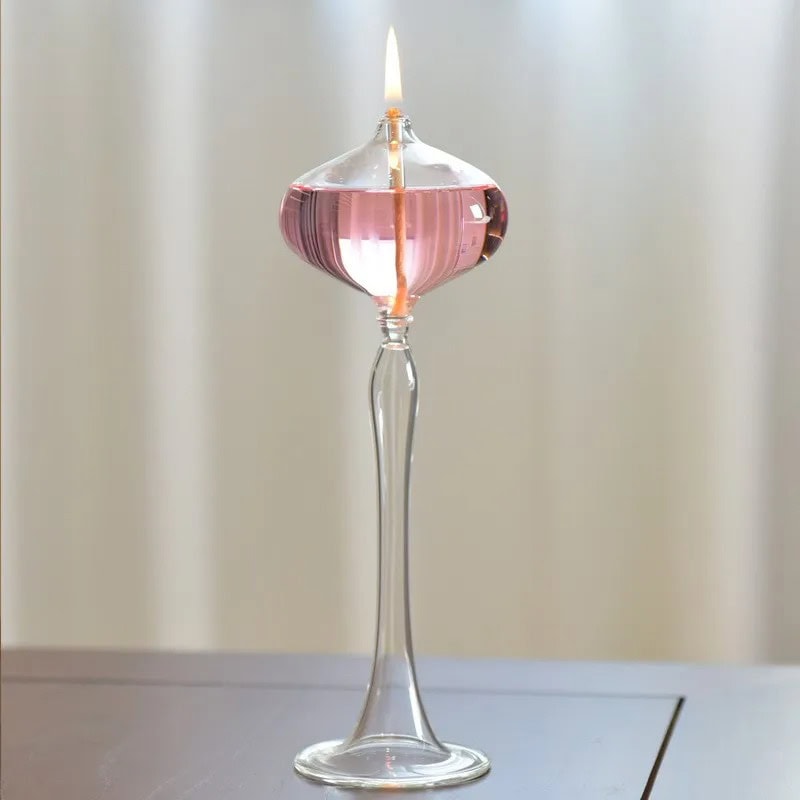 Candeeiro a Óleo de Pé Rosa Candeeiro a óleo de pé com base de vidro transparente, vela acesa e recipiente rosa, decorativo e funcional.