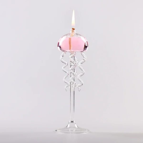 Candeeiro a óleo com design de medusas em vidro transparente, com chama acesa, colocado sobre uma base de vidro.