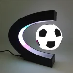 Luminária com estrutura em forma de C preta, iluminação LED colorida e bola de futebol em destaque no centro.