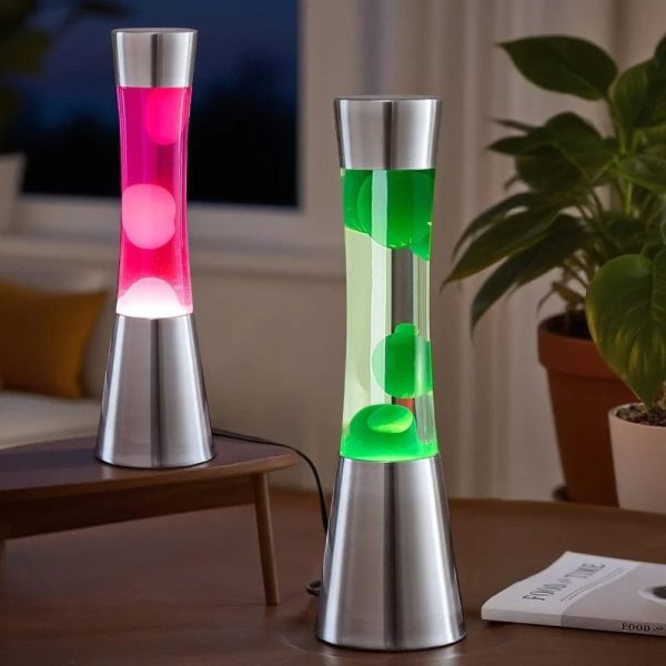 Duas lâmpadas de plasma em vidro com base metálica, uma com luz rosa e outra com luz verde, em ambiente interior com plantas e janela ao fundo.