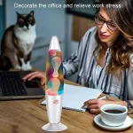 Lâmpada de plasma com cores vibrantes em ambiente de escritório, com uma mulher a trabalhar e um gato ao fundo.