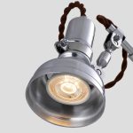 Lâmpada de mesa com estrutura metálica, braço articulado e fio de tecido castanho, iluminação acesa com foco ajustável.