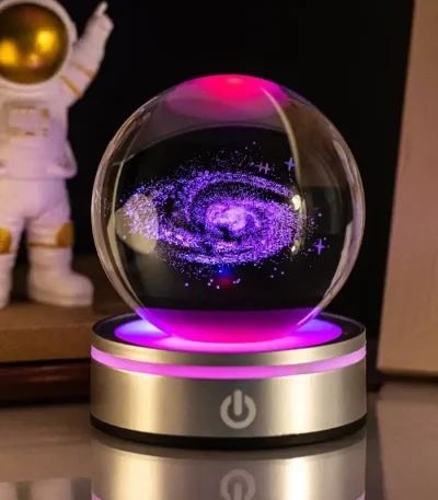 Globo de plasma com efeito de galáxia em movimento, luzes roxas e azuis, sobre base dourada com botão de energia, ao lado de figura de astronauta de brinquedo.