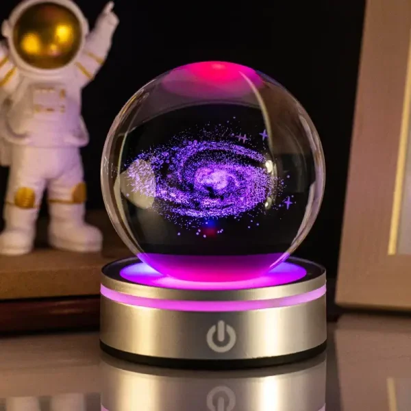 Globo de plasma com efeito de galáxia em movimento, luzes roxas e azuis, sobre base dourada com botão de energia, ao lado de figura de astronauta de brinquedo.