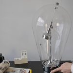 Lâmpada de plasma grande com tubo de vidro transparente, eletrodo metálico e base de suporte, usada para demonstrações científicas.