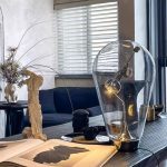 Lâmpada de mesa com design de lâmpada tradicional, com filamento visível e base de suporte preto, colocada numa mesa de sala moderna com decoração minimalista.