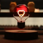Lâmpada de filamento com coração de néon aceso, refletindo luz quente, com fundo escuro e elementos desfocados ao fundo.