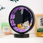 Espelho redondo decorativo com moldura de cristais de ametista roxa, refletindo objetos de decoração e uma parede escura ao fundo.