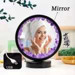 Espelho decorativo com luzes de ametista roxa ao redor, refletindo uma mulher sorridente com touca de banho branca, em ambiente de spa ou quarto.
