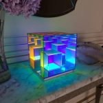 Luminária de mesa com cubos de acrílico iluminados em várias cores, criando efeito de luzes vibrantes e ambiente moderno.