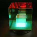 Luminária de vidro com três cubos iluminados em diferentes cores, incluindo vermelho, azul e verde, com iluminação interna que realça as cores vibrantes.