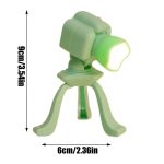 Luminária de mesa com design de câmara fotográfica, luz LED branca, corpo em plástico verde, base de três patas curvadas, tamanho compacto.