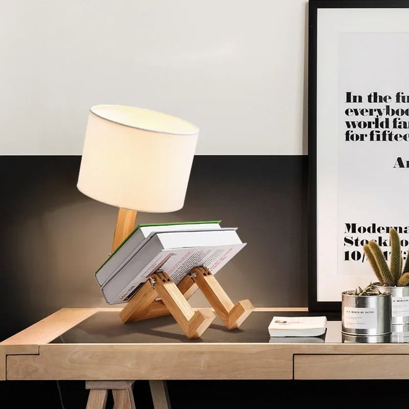 Luminária de mesa em madeira com design criativo Luminária de mesa com base de madeira em forma de robô, com abajur branco, colocada numa secretária de escritório moderna com quadro e plantas ao fundo.