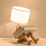 Luminária de mesa com base de madeira, lâmpada de tecido branco, apoiada em um suporte de forma criativa, ideal para decoração moderna e funcional.