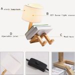Candeeiro de mesa com base de madeira, abajur de tecido, fonte de luz E27, e suporte ajustável em forma de pernas de boneco.