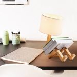 Luminária de mesa em madeira com abajur de tecido, suporte ajustável e iluminação suave, colocada numa secretária com livros e objetos de escritório.