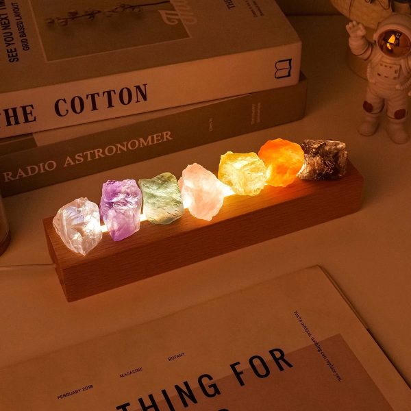 Lâmpada decorativa em pedra com várias cores, iluminada, colocada numa base de madeira, com livros e figura de astronauta ao fundo.