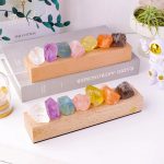 Cristais de vários tamanhos e cores, incluindo branco, roxo, azul, rosa, amarelo, laranja e preto, dispostos em duas bases de madeira em diferentes ângulos.